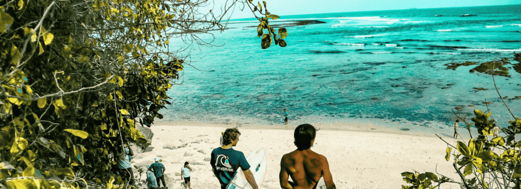 Three figures walk towards the ocean along a picturesque path, framed by lush greenery and a bright sky.