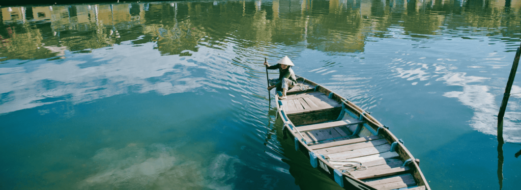 A man rowing a boat on a serene river, surrounded by lush greenery and calm waters.