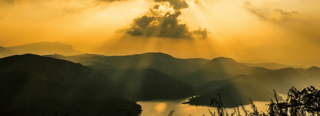 Sunbeams illuminate the mountain peaks as clouds drift above, creating a serene and picturesque landscape.