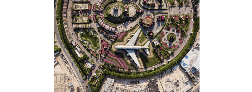 Aerial view of a lush garden featuring vibrant flowers and greenery, with a small plane flying above.