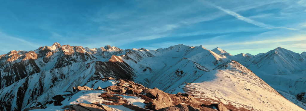 A panoramic view of majestic mountains from the summit, showcasing peaks and valleys under a clear blue sky.