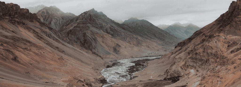 A serene river meanders through a majestic canyon surrounded by towering mountains under a clear blue sky.