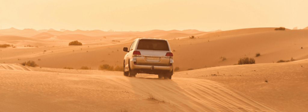 A white SUV navigating through sandy terrain in a sunlit desert environment.