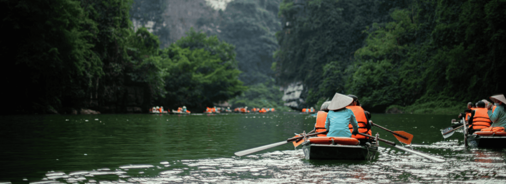 A gathering of individuals in boats gliding along a tranquil river, framed by vibrant natural scenery.