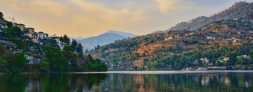 A serene lake bordered by majestic mountains and quaint houses, reflecting the beauty of nature and human habitation.