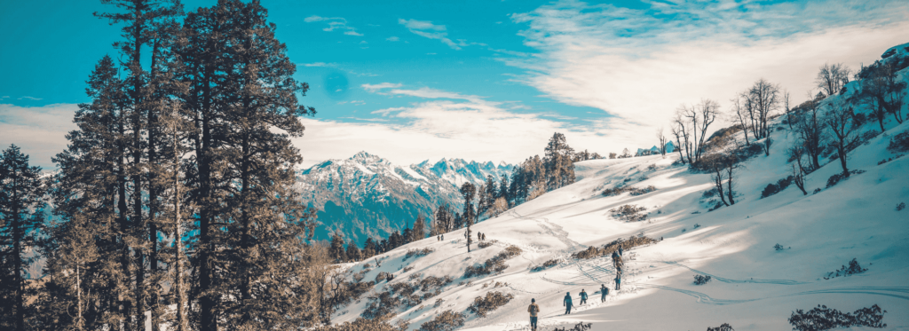 Scenic view of snow-covered mountains and trees, featuring individuals walking on the mountain's side.
