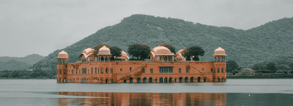 A large building on the water's edge, framed by majestic mountains in the background, showcasing a serene landscape.