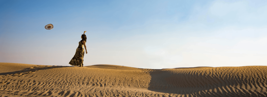 A woman stands gracefully on the sandy beach, with the ocean waves gently lapping at her feet.